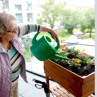 Betagte Frau waessert Blumen auf Balkon